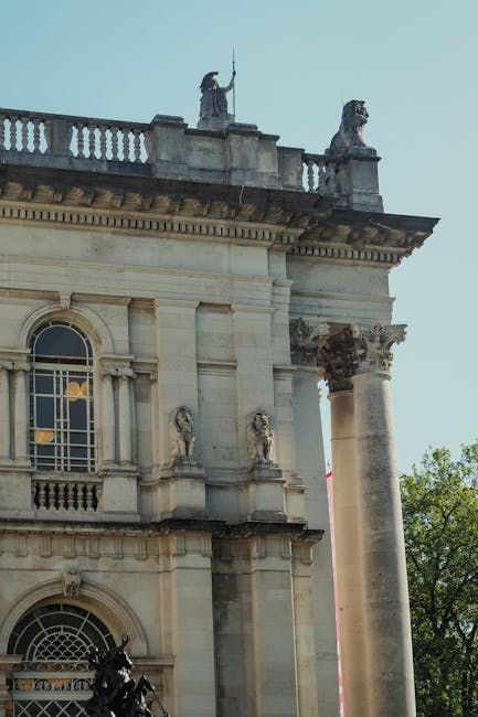The image shows the upper section of a historic classical building with ornate architectural details, including decorative columns and stone sculptures. Prominently visible are two stone lion statues 